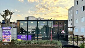 A modern building with large glass windows, a paved area with a bench, and a signboard advertising a market.