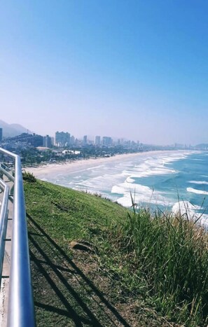 Un paysage urbain côtier avec une plage, un ciel dégagé et une silhouette urbaine lointaine.