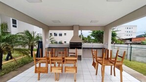 An outdoor patio with a tiled floor, wooden chairs, and a grill area.