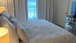 Een slaapkamer met een bed, een plafondventilator, een dressoir en uitzicht op de oceaan.