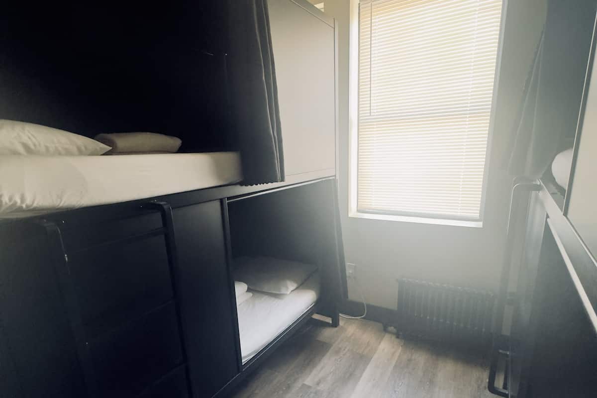 A small, compact room with a bunk bed, a window with blinds, and a radiator.