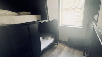 A small, compact room with a bunk bed, a window with blinds, and a radiator.