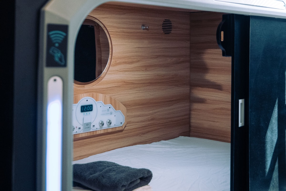 A compact, modern sleeping area with a bunk bed, a control panel with a digital clock, and a small circular window.