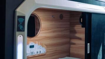 A compact, modern sleeping area with a bunk bed, a control panel with a digital clock, and a small circular window.