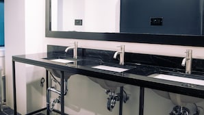 A modern bathroom with two sinks, a large mirror, and a black countertop. - Kama Central Park Hostel (New York)
