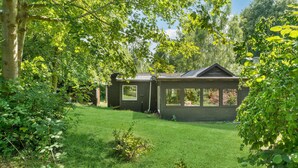 Two small, dark-colored cabins with large windows, surrounded by lush green grass and trees. - 2 bedroom amazing home in Jægerspris (Jægerspris)