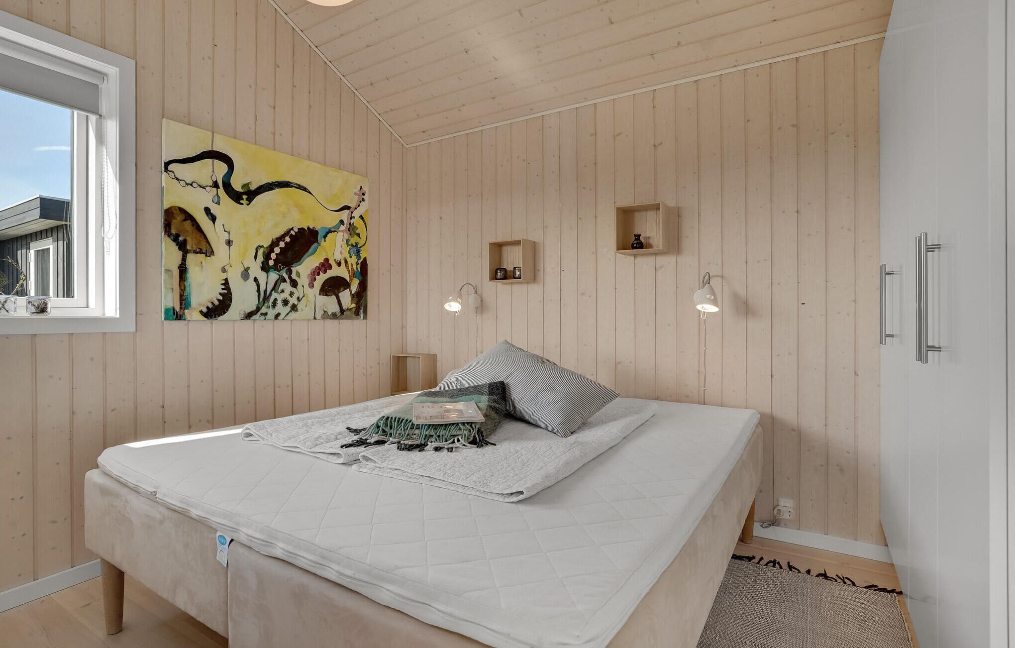Ein Schlafzimmer mit Bett, Fenster, Holzwänden, einem Gemälde und Nachttischen.
