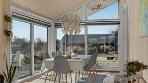 A modern dining area with a glass table and chairs, large windows, and a view of the outdoors.