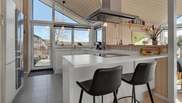 A modern kitchen with a large island, two bar stools, and a view of the outdoors.