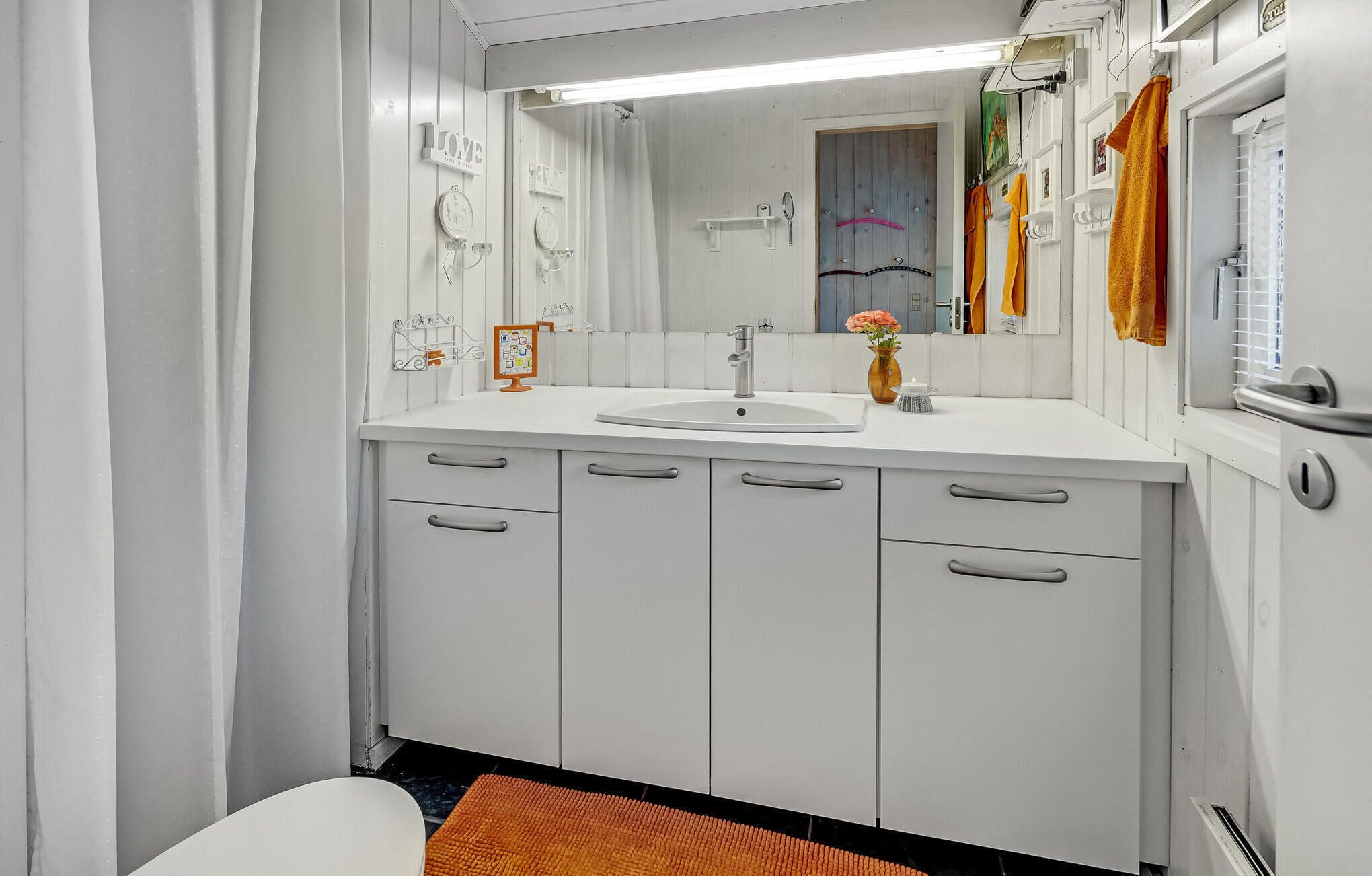 Un baño con un lavabo blanco, espejo y armarios. Hay toallas colgadas en la pared y una cortina de ducha.