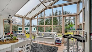 A spacious room with large windows, a white sofa, a dining table, and a kitchen area. - Lovely home in Hals with kitchen (Hals)