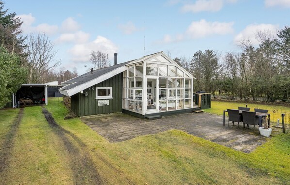 A glasshouse with a roof, a small attached shed, and a patio area with outdoor furniture.
