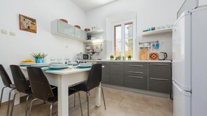 Een moderne keuken met een eetgedeelte, met een witte tafel, zwarte stoelen en grijze kastjes.