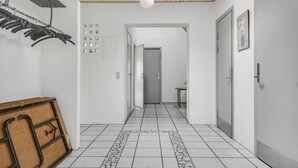 A hallway with a tiled floor, a coat rack, a suitcase, and a door leading to another room.
