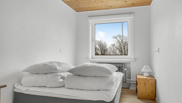 A bedroom with a bed, a window, a radiator, and a bedside table.