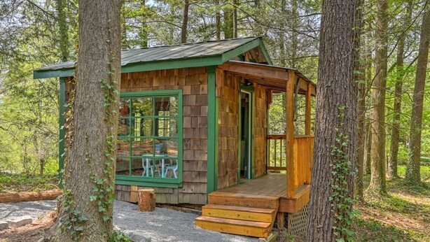 Una pequeña cabaña de madera con un porche, rodeada de árboles.