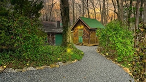 Una cabaña rústica con un sendero de grava que lleva a ella, rodeada de un bosque denso.