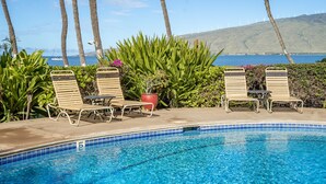 A poolside area with lounge chairs, a potted plant, and a view of the ocean and wind turbines. - Awesome Oceanfront Condo, Great Views, Steps to the Beach, KR#207 (Kihei)