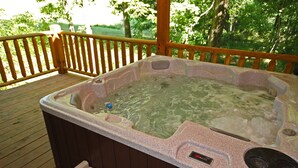 A hot tub on a wooden deck with a wooden railing, surrounded by greenery. - Piccolo - Sweet Couple's cabin in Hocking Hills (Logan)