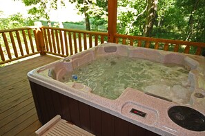 A hot tub on a wooden deck with a wooden railing, surrounded by greenery. - Piccolo - Sweet Couple's cabin in Hocking Hills (Logan)