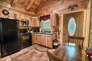 Une cuisine rustique aménagée dans une cabane en bois, avec un réfrigérateur noir, un four à micro-ondes, des placards en bois, une table à manger en bois et une porte en vitrail.