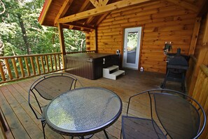 Una terraza de madera con jacuzzi, parrilla y sillas de metal.