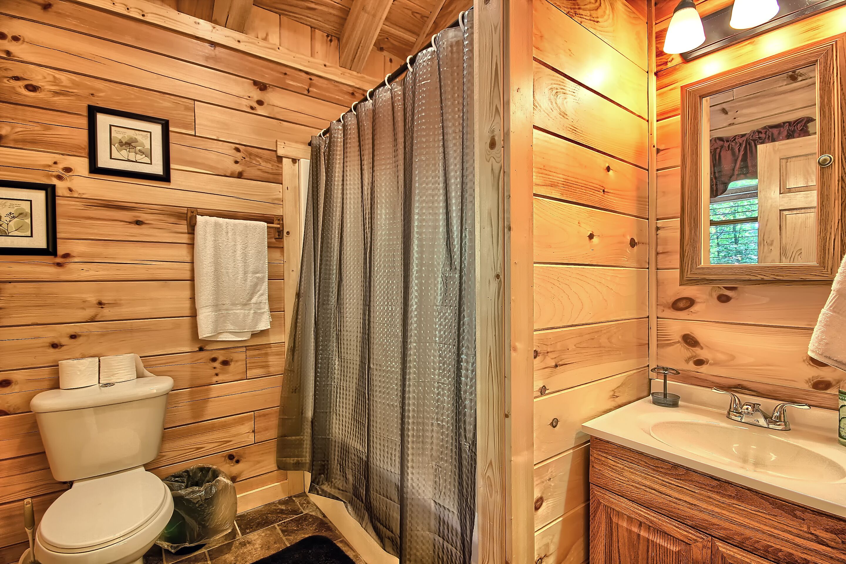 A wooden bathroom with a toilet, sink, and shower curtain.