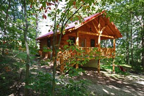 A wooden cabin with a porch, surrounded by trees.
