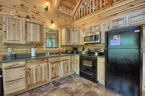 A wooden cabin kitchen with a black refrigerator, stainless steel microwave, and a gas stove.