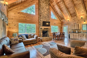 L’intérieur d’une cabane en rondins, avec une cheminée en pierre, des meubles en bois et de grandes fenêtres.