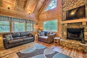 Ein gemütliches Blockhaus mit Kamin aus Stein, Holzwänden, einer Ledersofa und einem Fernseher, der über dem Kamin angebracht ist.