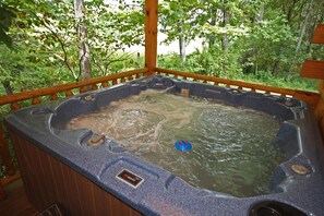 A hot tub with a wooden deck and a view of a forested area.
