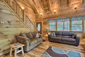 A cozy cabin interior with wooden walls, a staircase, two leather sofas, a small table, and a rug.