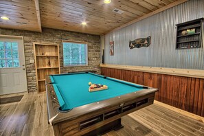 Ein Billardtisch mit Kugeln, eine Steinwand, Holzregale und eine Tür.