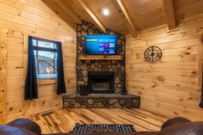 A cozy cabin interior with a stone fireplace, wooden walls, a mounted TV, and a clock on the wall. - Snuggle Inn - Cozy Couple's Cabin in Hocking Hills (Logan)