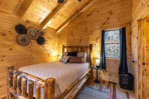 A wooden cabin bedroom with a bed, a window with curtains, and a wall-mounted lamp.