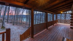 Une terrasse en bois dotée d’une balustrade, offrant une vue sur une zone boisée, avec des arbres et une chaîne de montagnes lointaine.