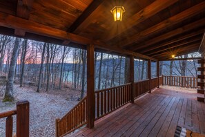 A wooden deck with a railing, overlooking a forested area with a view of trees and a distant mountain range.