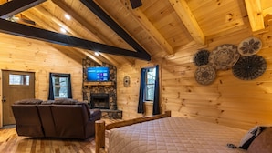 L’intérieur chaleureux d’un chalet en bois comprend un lit, un canapé, une cheminée et un téléviseur fixé au mur.