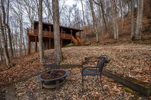 A cabin with a deck and a fire pit area with two chairs.