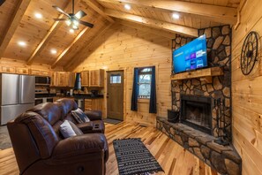 A cozy cabin interior with a stone fireplace, wooden walls, a leather sofa, and a mounted TV.