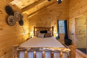 A wooden cabin bedroom with a bed, pillows, a nightstand, wall decor, and a window.