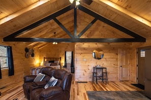 A wooden cabin interior with a loft bedroom, a living area with a leather sofa, and a dining area.