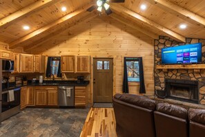 Une cabane en rondins comprenant une cuisine, un coin repas et une cheminée.