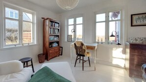 Een kamer met een bed, een bureau, een stoel, een boekenkast en grote ramen.