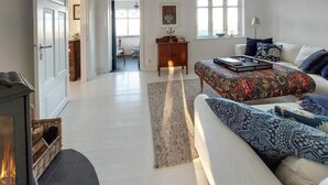 Een ruime woonkamer met een grote bank, een vloerkleed met patroon en een open haard.