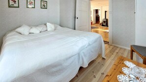 A bedroom with a large bed, a wooden floor, and a door leading to a kitchen area.
