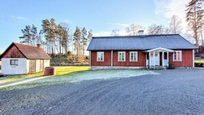 A red wooden house with a grey roof, a small attached shed, and a gravel driveway.