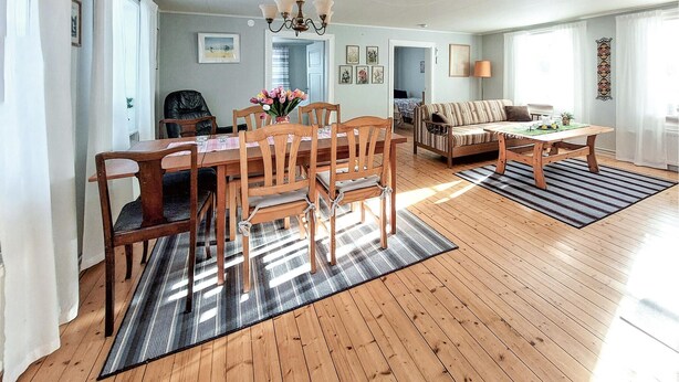 A spacious living room with a wooden floor, a sofa, a coffee table, and a dining area with wooden chairs and a table.