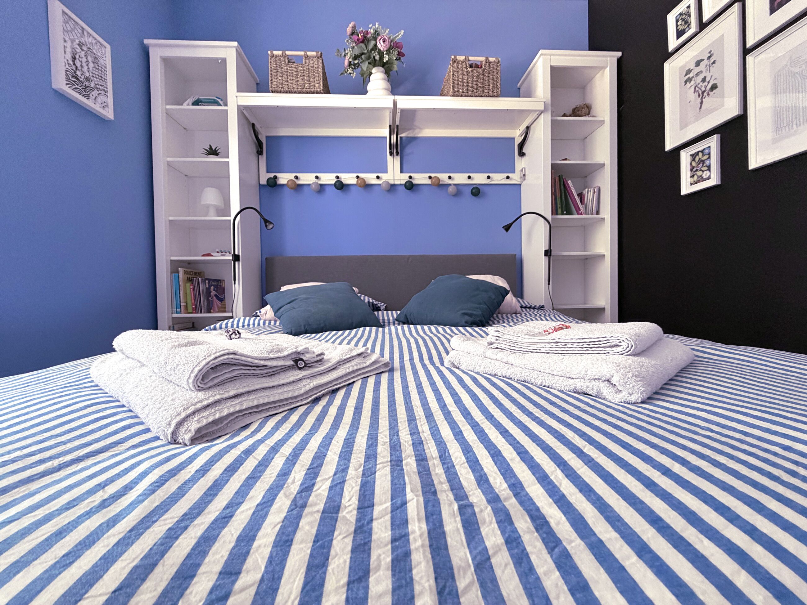 Ein Bett mit gestreifter Bettwäsche, ein Kopfteil mit Ablagen und eine Wand mit gerahmten Bildern.
